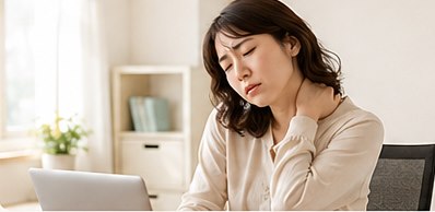 デスクワークの合間に首の後ろへ手をやり、肩の重さをこらえている女性